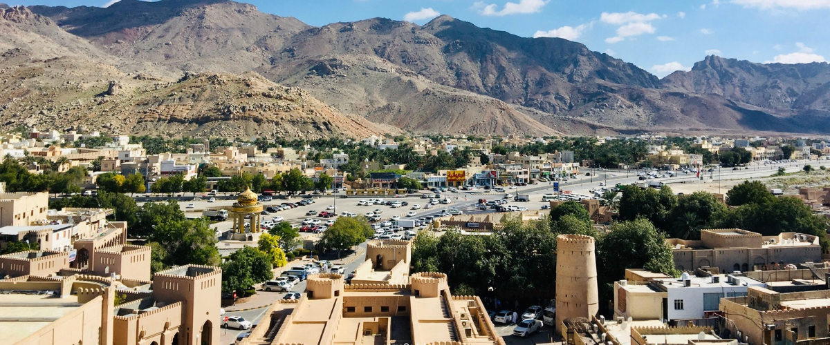 منظر عام لمدينة نزوى وبرج القلعة الدائري أمام جبال الحجر في سلطنة عمان