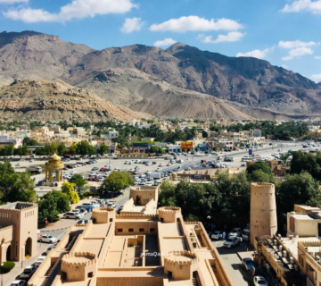 منظر عام لمدينة نزوى وبرج القلعة الدائري أمام جبال الحجر في سلطنة عمان
